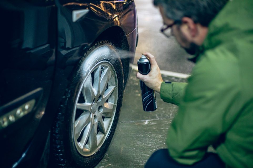 A man spraying wheel cleaner on a wheel of a black car.