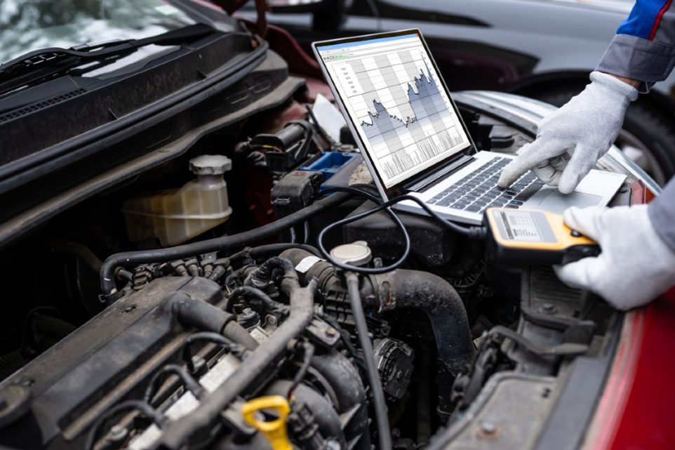 A mechanic using the MOTOPOWER Car Diagnostic Tool while looking under the hood of a car.