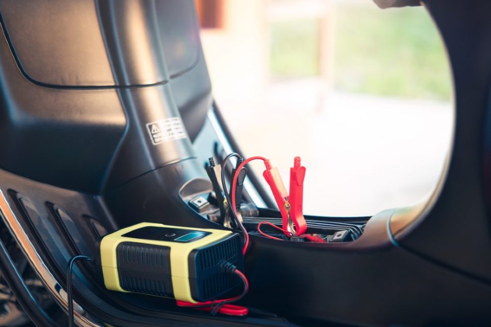 A car jump starter is securely attached to a car battery with clamps.